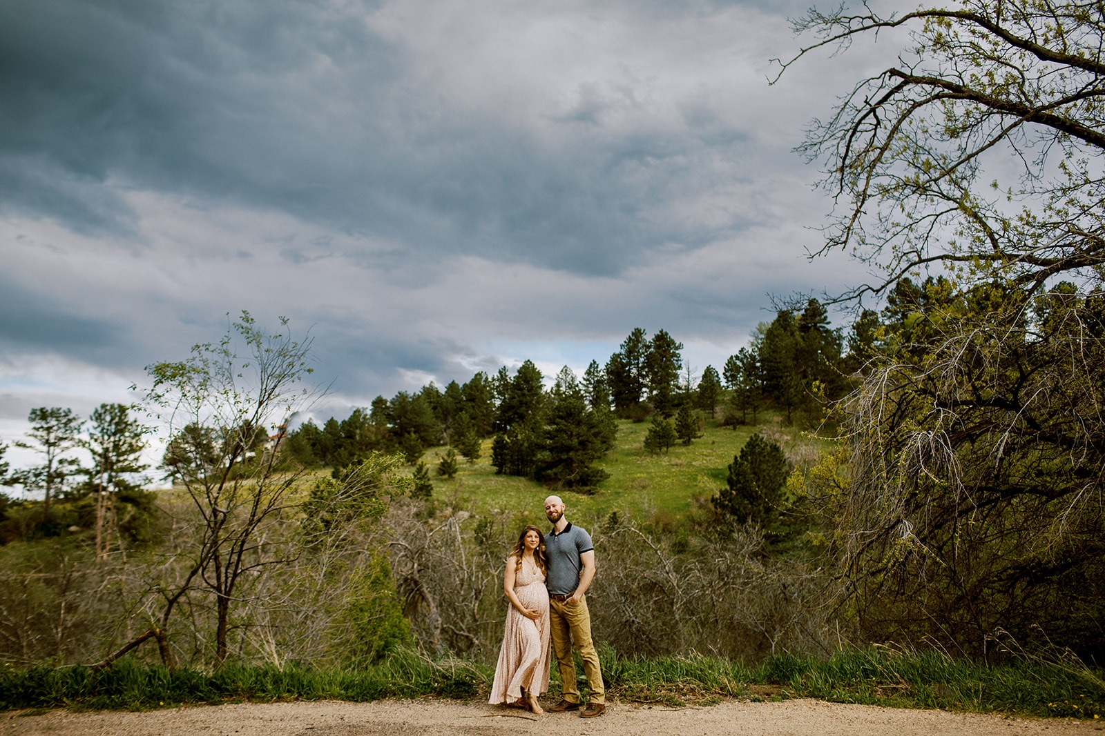 pregnant woman and partner stand in front of green hill in boulder, colorado