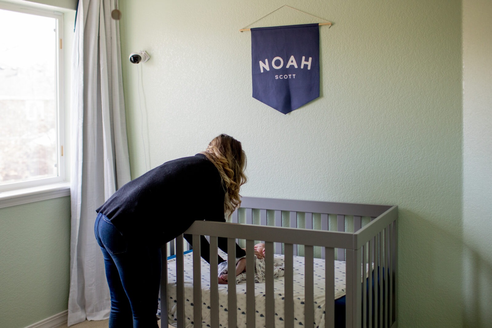 a mom tucks her newborn baby into his crib