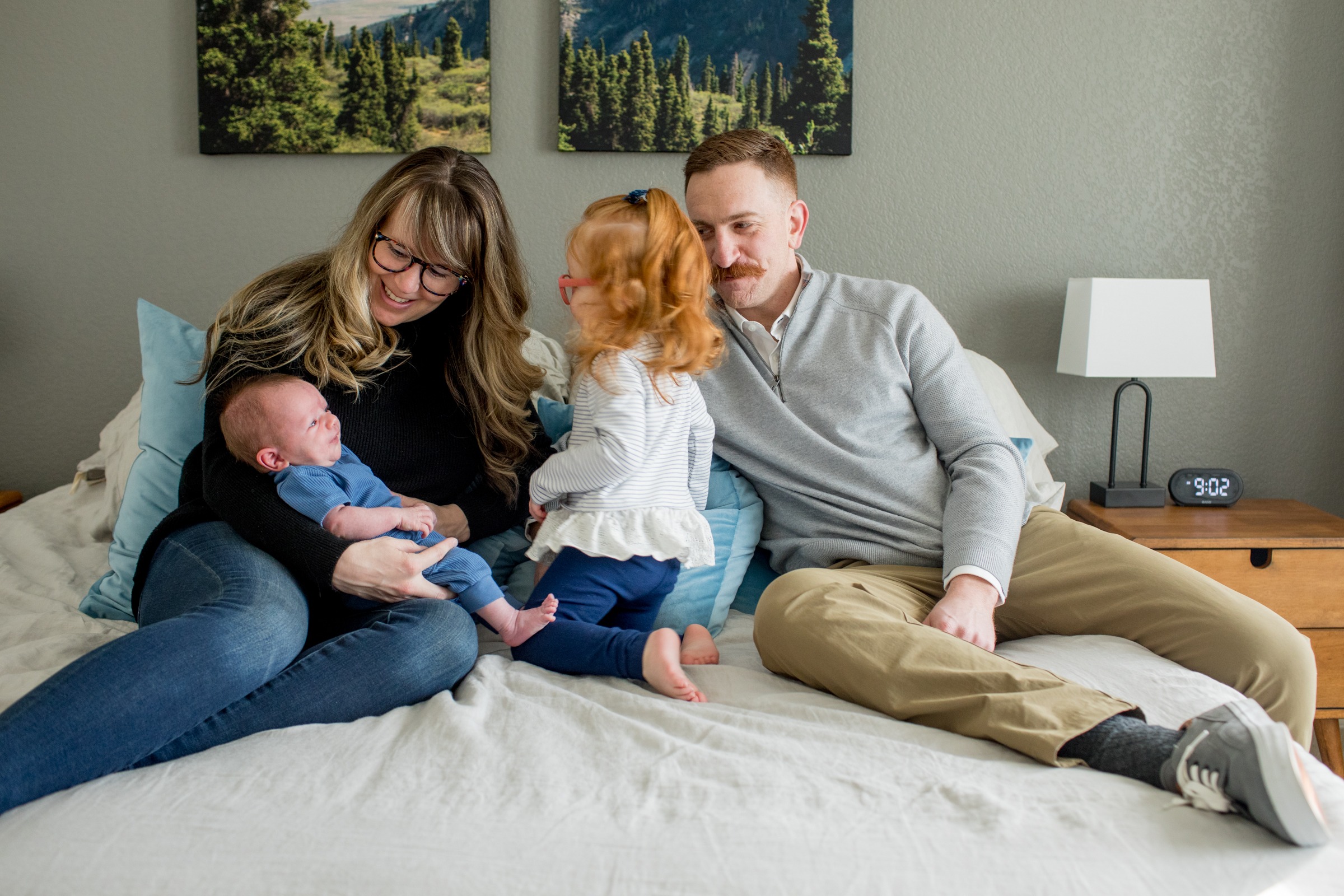 family sits on bed and looks at newborn baby boy
