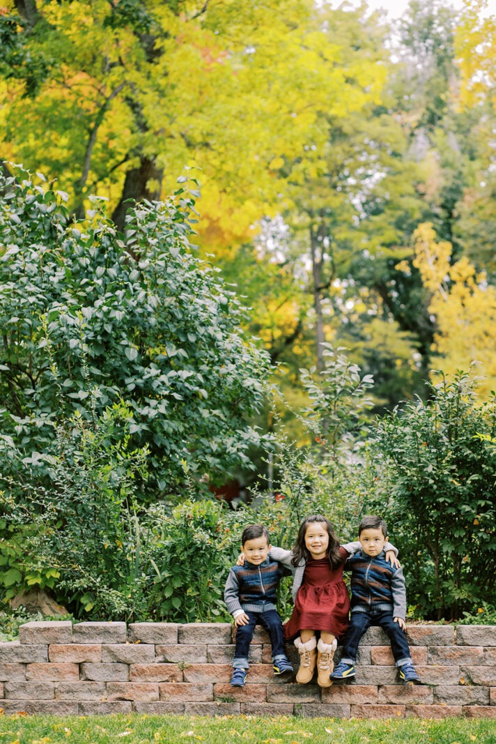 Colorado fall family photos at Thompson Park in Longmont featuring three siblings sitting on a brick wall
