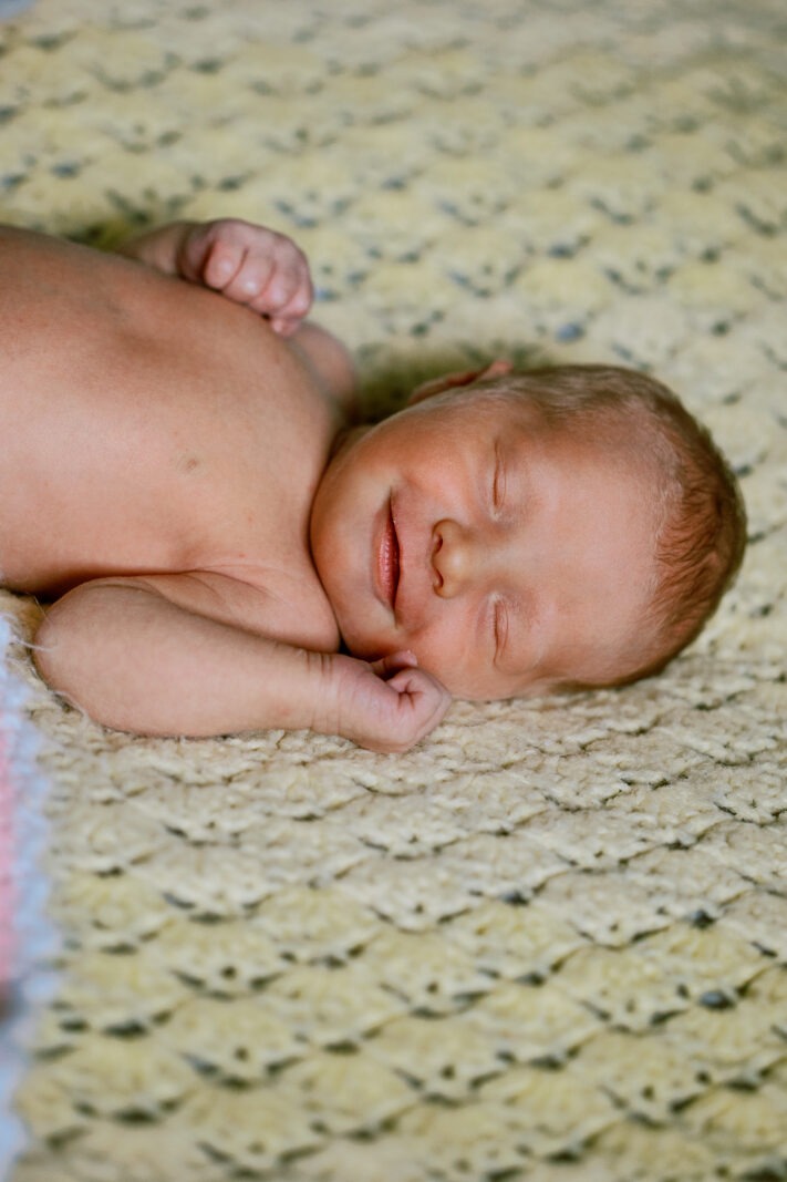 a baby sleeps on a comfy blanket and wears a small smile during a luxury newborn photography session