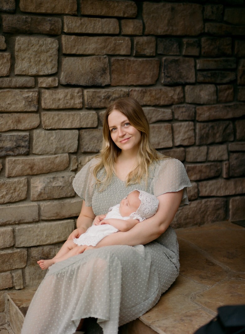 mom in green dress holds baby girl in white during a luxury newborn baby session in longmont, colorado