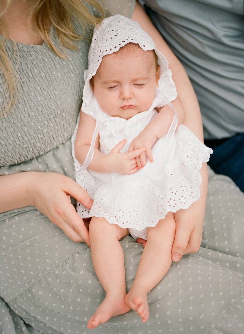 a close up of a baby girl wearing a white dress and white hat during a longmont colorado baby photoshoot