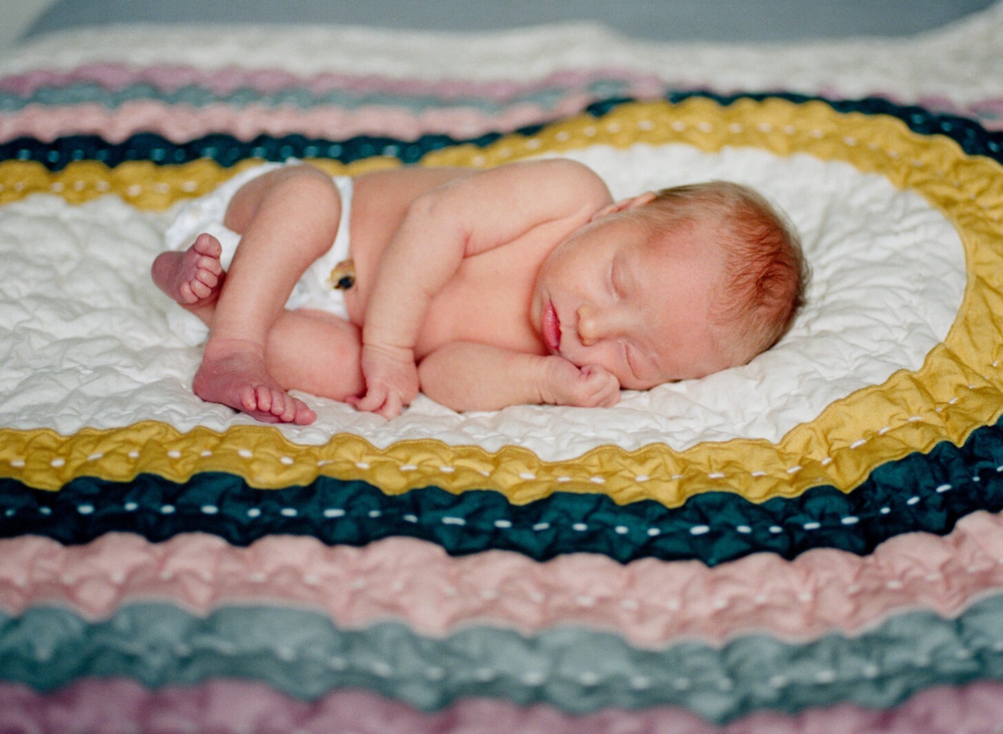 sleeping baby curls up on a nice comforter during a newborn photography session