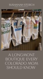 Locally inspired “Hugs from Longmont” baby onesies hanging on a brick wall inside Adornables, a woman-owned boutique in Longmont, Colorado, offering sustainable and community-focused baby gifts.