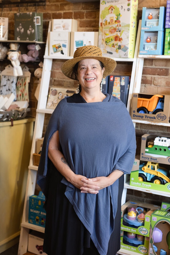 Sharald, owner of Adornables boutique in Old Town Longmont, stands in front of a display of sustainable wooden toys and organic baby clothes inside her children’s shop.