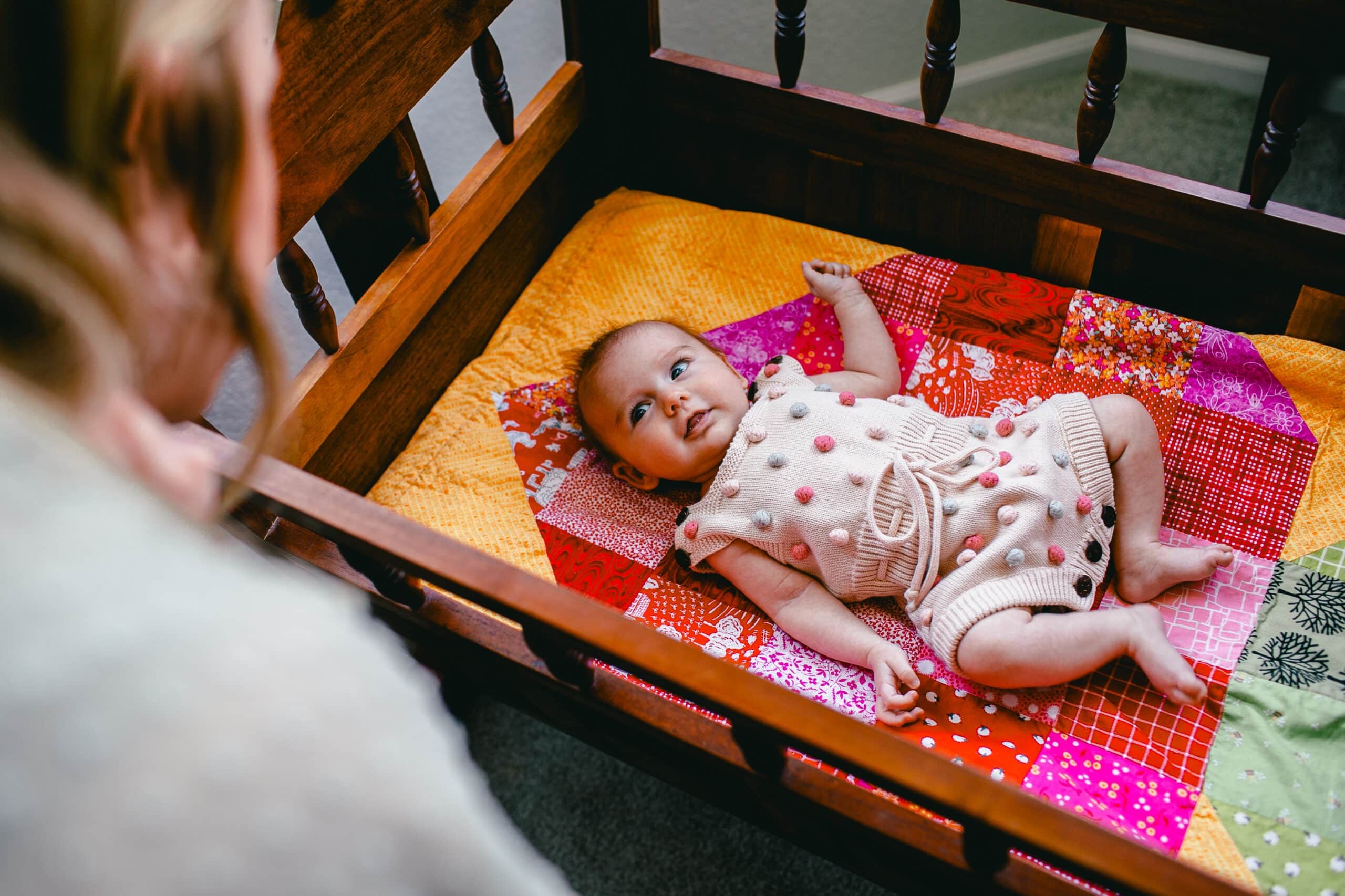 baby looks at mom while lying in family heirloom crib during longmont in-home newborn photography portrait session