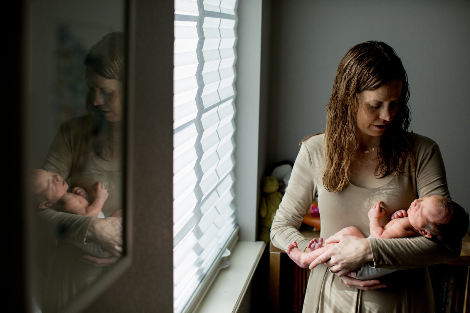 mom looks at new baby boy near a window during a colorado in-home newborn photography session