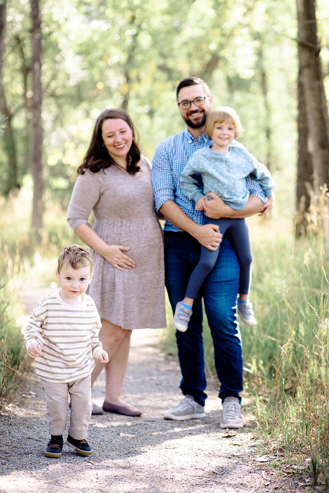 family of four with pregnant mom holding belly during spring photo session in Berthoud Colorado