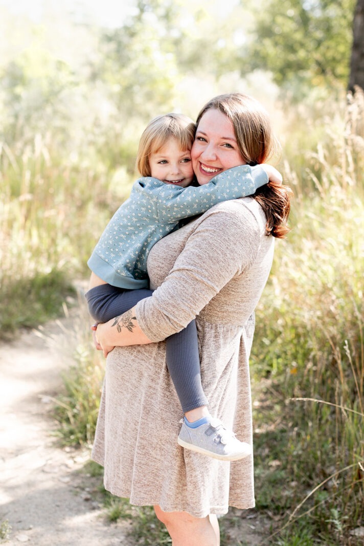 mom holding child in tall grass during spring photo session in Longmont Colorado